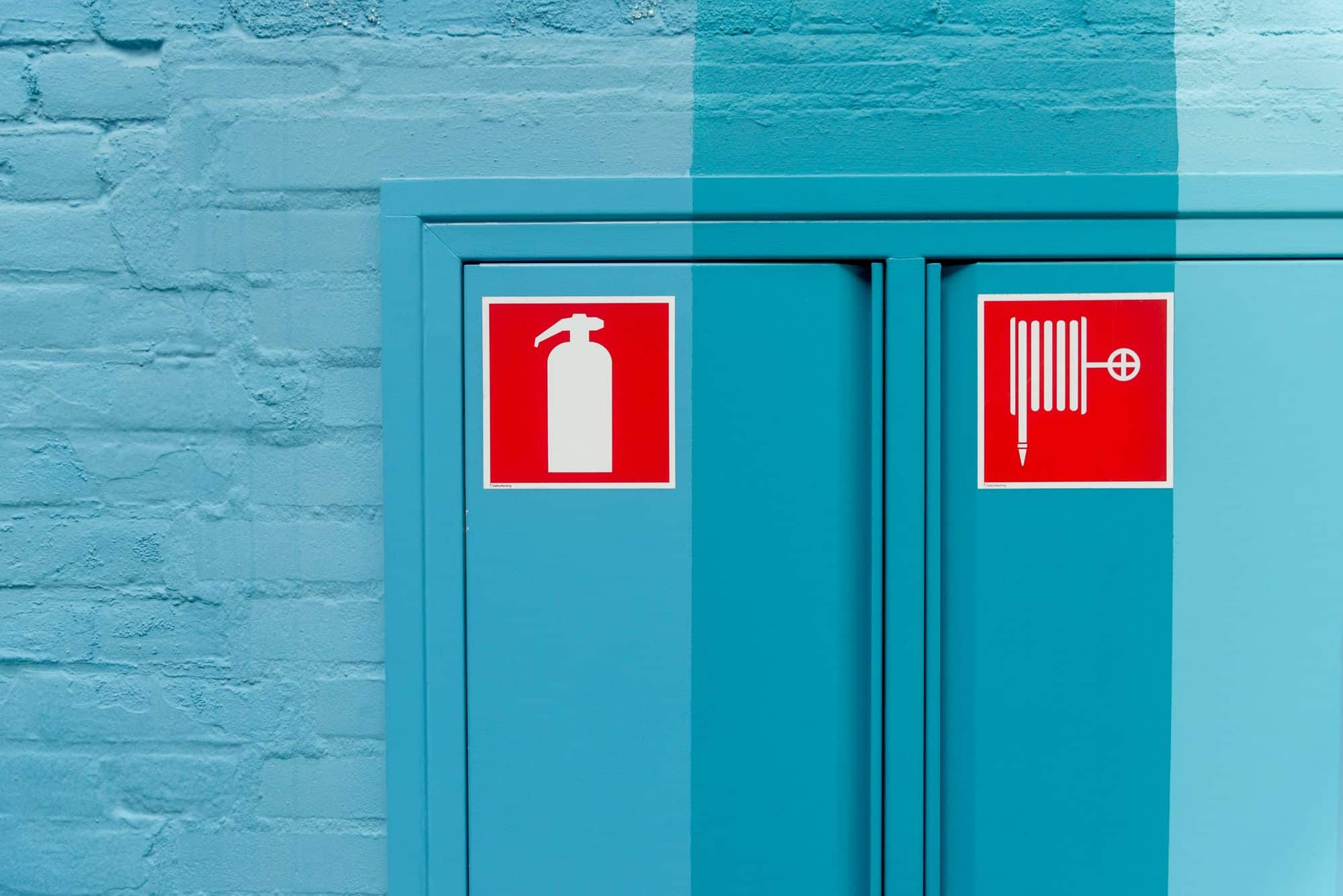 Fire extinguisher and fire hose reel safety signage mounted on a workplace wall, part of a compliant business signage system